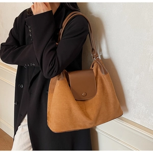 Detail view of a large brown suede shoulder bag featuring leather trim on model