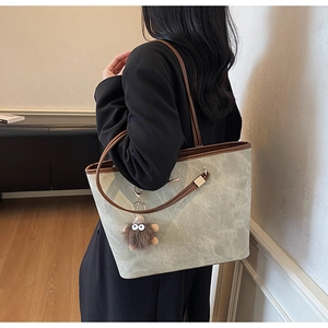 Detail of grey marble textured tote bag with brown straps and cute plush monster pendant