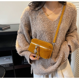 Détail du sac bandoulière jaune mat avec breloque robot et pompon sur tricot beige