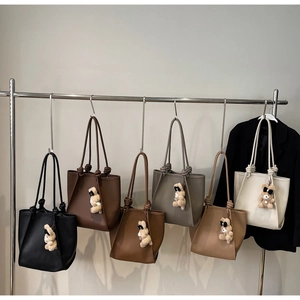 Detail of five leather tote bags in various colors with knotted handles and bear charms