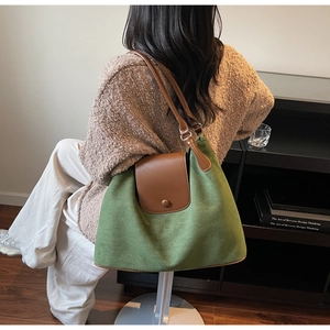 Detail view of large green suede tote bag with brown leather trim in home setting