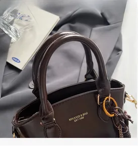 Detail of glossy chocolate brown faux leather tote bag with gold logo and round handles