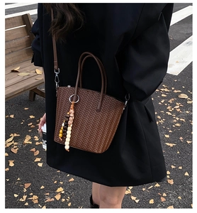 Brown woven trapezoid bucket bag with bead charm shown in an autumn street style scene