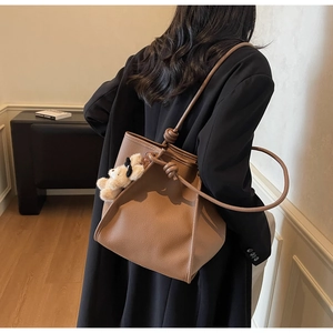 Close-up of caramel leather tote bag featuring unique knot details and a plush bear charm