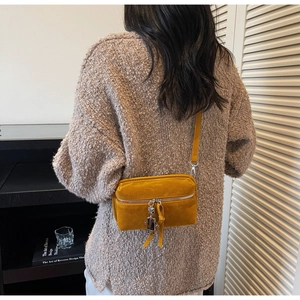 Detail of yellow suede crossbody bag with silver robot charm and front zipper compartment