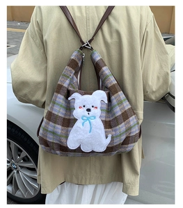 Detailed view of plaid tote bag featuring a white cartoon dog patch and brown leather strap
