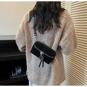 Detail of black suede crossbody bag featuring silver zipper and robot charm on sweater