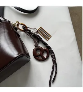 Detail of dark brown glossy leather bag with gold abacus and woven rope charms