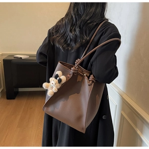 Detail of dark brown pebble leather tote bag with a plush bear charm and knotted shoulder strap