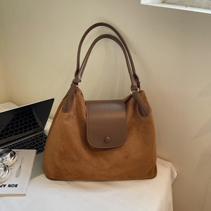 Detail of a large brown suede tote bag with leather flap in a professional office setting