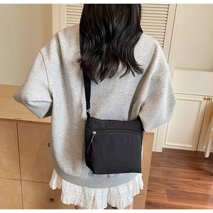 Detailed view of the black canvas crossbody bag with front zipper pocket on a model
