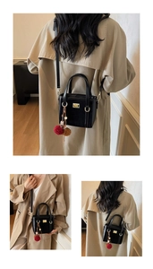 Detail view of black textured leather handbag with gold hardware and colorful pompom charm