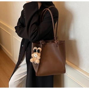Detail view of brown pebbled leather tote bag with knotted straps and bear charm