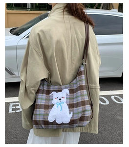 Detail of checkered tote bag with plush puppy patch worn by model in outdoor setting