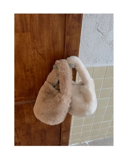 Detailed close-up of plush faux fur bucket bags in beige and khaki hanging on a wood door