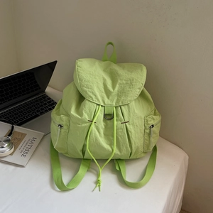 Detalle de mochila de nylon verde neón con cordón y bolsillos laterales en escritorio