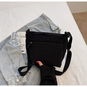 Detail view of black nylon crossbody bag featuring sturdy zipper and woven strap