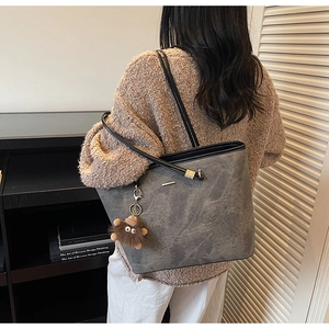 Detailed view of grey tote bag with fuzzy charm on model in cozy home setting