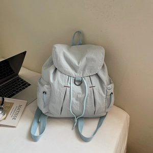 Detalle de la mochila de nailon azul claro con cierre de cordón y solapa con anillo de metal