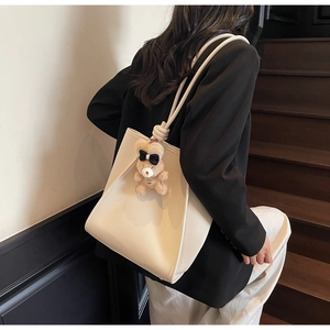 Detail of minimalist cream tote bag with litchi grain leather and cute brown bear charm