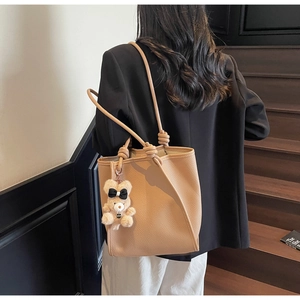 Detail view of light brown pebbled leather tote bag with knotted handles and bear charm