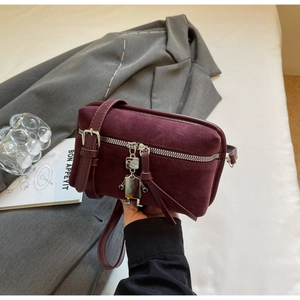 Close-up of wine red suede box bag featuring unique metal robot charm and silver zippers