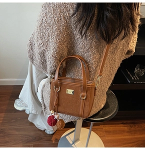 Detailed view of a brown leather bucket bag with plush charm and gold logo plate