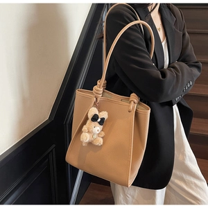 Detail of a brown leather tote bag with a unique knotted shoulder strap and bear charm