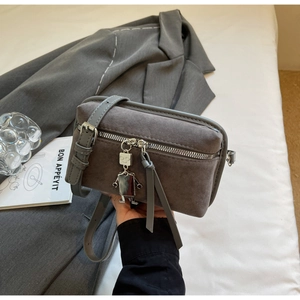 Detail of grey suede crossbody box bag with silver zippers and robot charm pendant