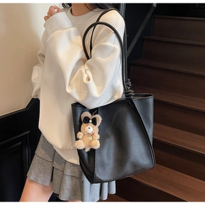 Detail of black pebbled leather tote bag with knot strap and cute brown plush bear charm