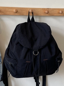 Mochila minimalista de nailon negro con cierre de solapa y detalle de anillo metálico