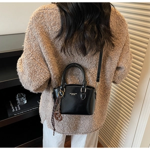 Detail of black patent leather crossbody bag with bow charm and branding text on a model