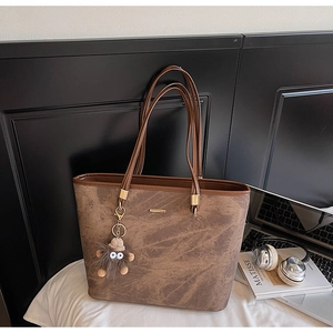 Detailed view of brown tote bag with fuzzy monster charm and office accessories