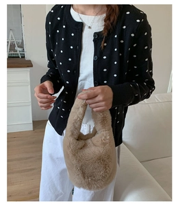 Detail of a fuzzy beige faux fur bucket bag held by a person in a polka dot cardigan