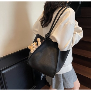 Close-up of black lychee grain leather tote bag with a cute teddy bear plush charm