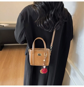 Detail of tan leather crossbody bucket bag with fuzzy pompom charm and gold hardware