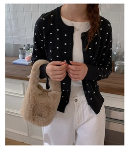 Close-up of a plush khaki bucket handbag paired with a black polka dot cardigan