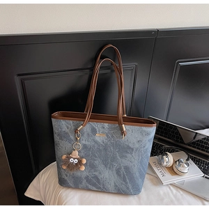 Detail of blue marble tote bag with brown leather straps and a fuzzy monster charm