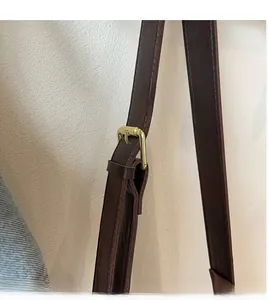 Close-up of dark brown leather shoulder strap with gold buckle and fine stitching detail