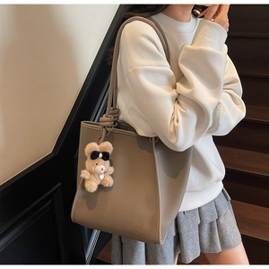 Detail of grey lychee leather tote bag with knot shoulder strap and plush bear charm