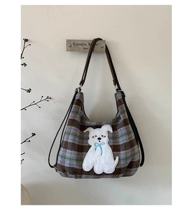 Detail of checkered hobo bag featuring white puppy embroidery and brown leather strap