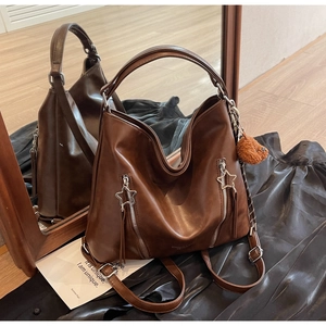 Detail of dark brown hobo bag featuring star zippers and a plush bear charm on silk