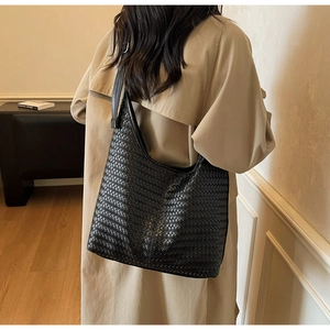 Détail de la texture d'un sac hobo en cuir tressé noir porté avec un trench-coat kaki