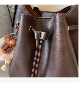 Detail of a dark brown pebble leather bucket bag with a drawstring closure and bear charm
