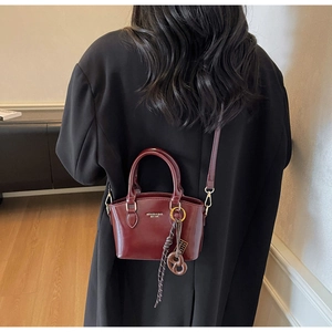 Detail of burgundy leather crossbody bag with artistic charm shown on a person