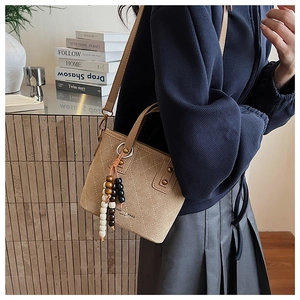 Détail du sac seau beige avec coutures matelassées et pompon en perles colorées