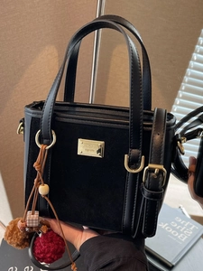 Fashionable black bucket bag with gold hardware and plush charm shown in a cozy setting