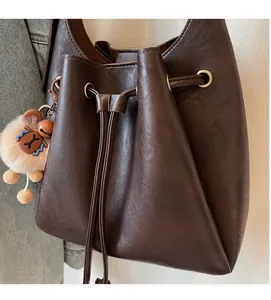 Detail of dark brown leather bucket bag featuring a drawstring closure and bear charm