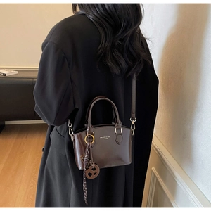 Detail view of coffee leather trapezoid handbag with dual handles and woven pendant