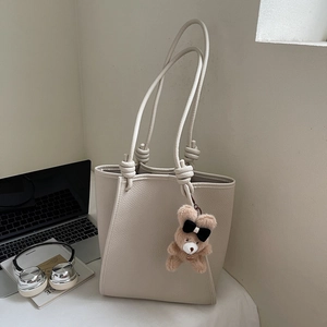 Detail of off-white lychee leather tote bag with brown plush bear charm and long straps